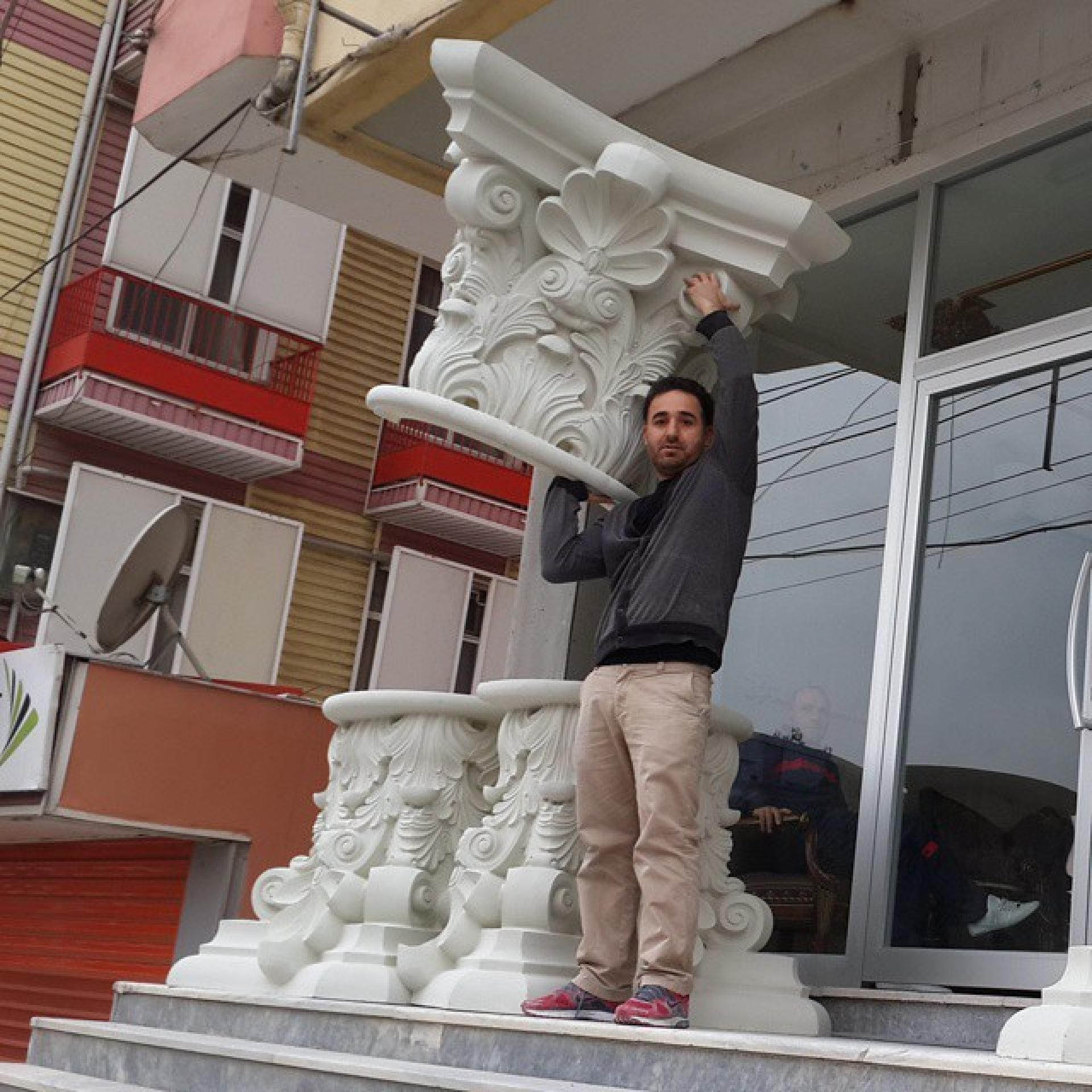 Bir ustanın omzunda hafifçe taşıdığı büyük boy poliüretan sütun başlığı ve yerdeki iki adet kaide modeli.
