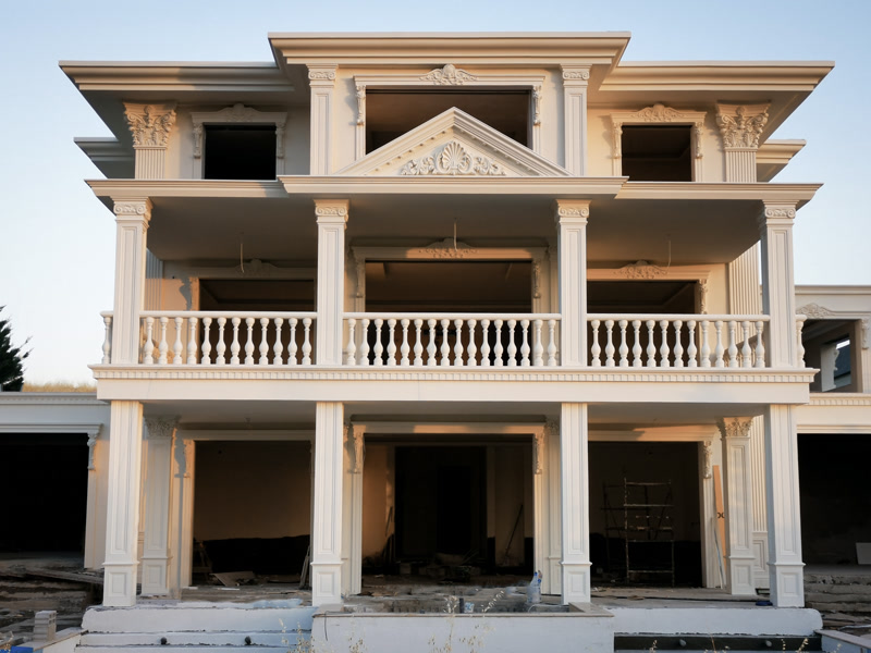 Poliüretan pilaster sütunlar, dekoratif taçlar ve söve kaplamaları ile süslenmiş klasik üç katlı beyaz villa cephesi.