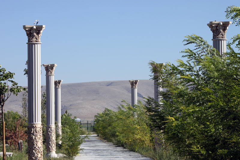 Kır bahçesinde yeşillikler ve dağ manzarası eşliğinde iki sıra halinde dizilmiş beyaz poliüretan sütunlar ve yürüyüş yolu.