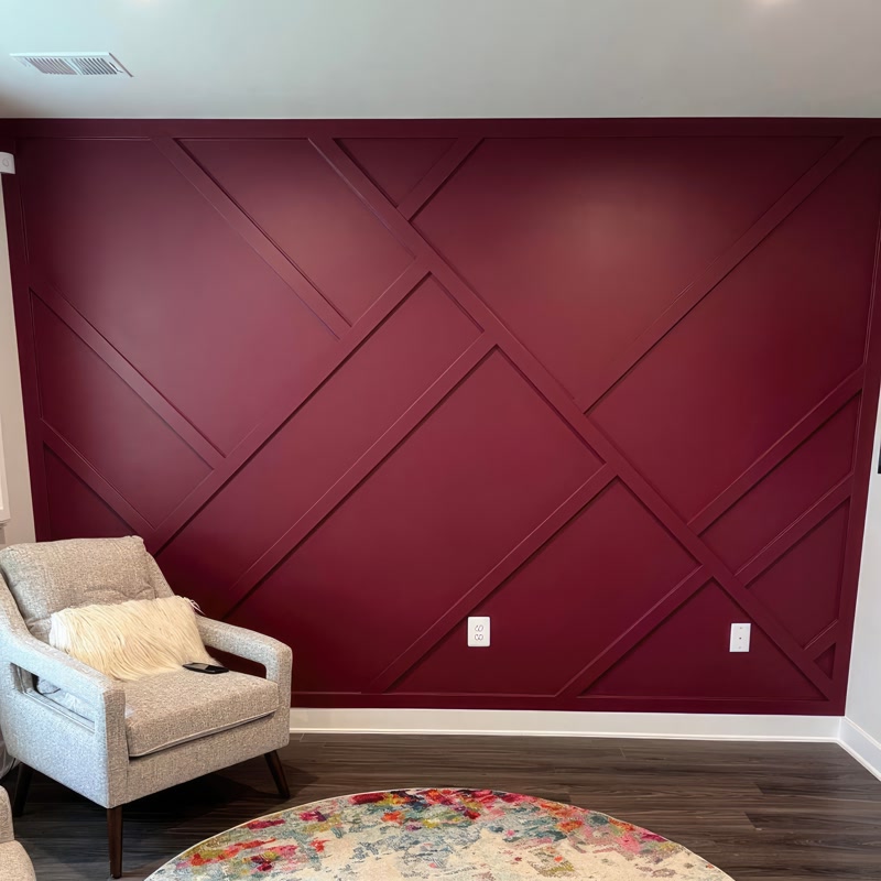 Bordo boyalı duvarda P851350 poliüretan çıtalarla yapılmış geometrik desen tasarımı ve önünde gri berjer koltuk.