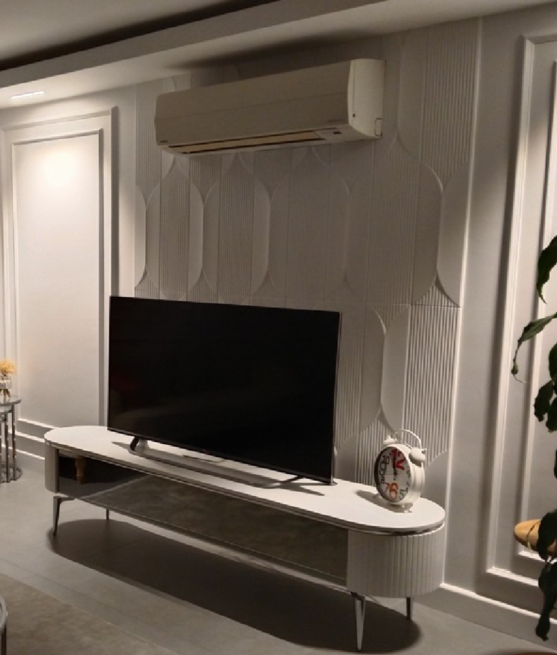 Beyaz TV ünitesi arkasında kavisli dikey çizgili poliüretan P312020 duvar paneli uygulaması ve modern salon dekoru.