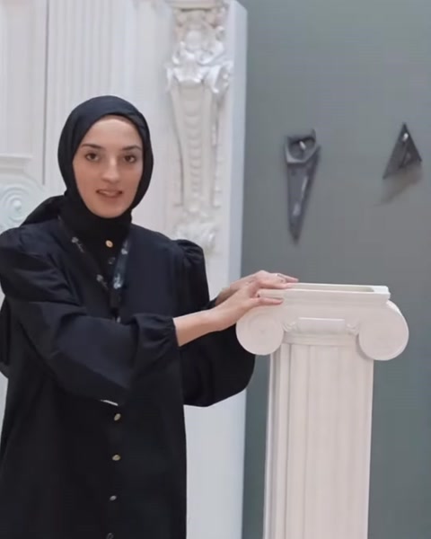 Sunucu kare tablalı kıvrımlı sütun başlığına eliyle işaret ediyor