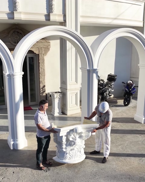 İki çalışan dışarıda tamamlanmış kemer ve sütun yanında parça taşıyor